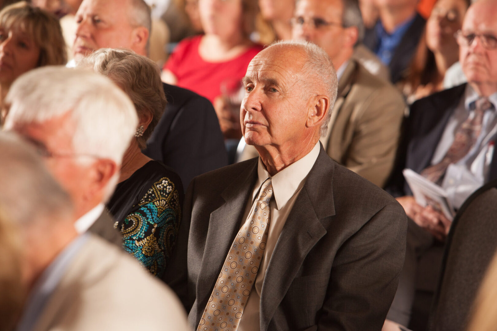 A man in suit and tie sitting next to other people.