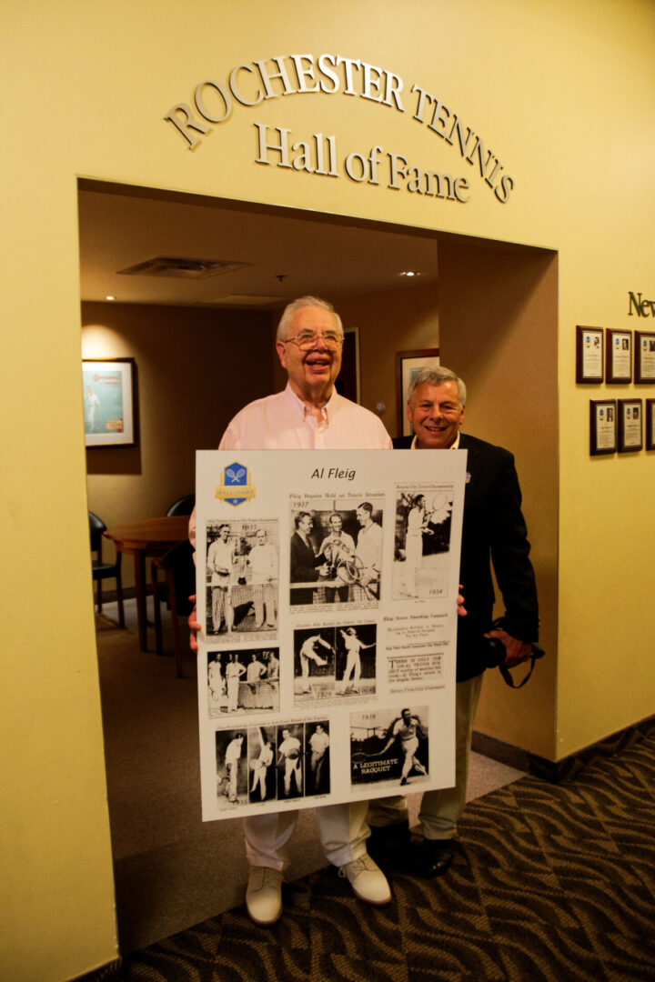 Two men holding a sign in front of a wall.