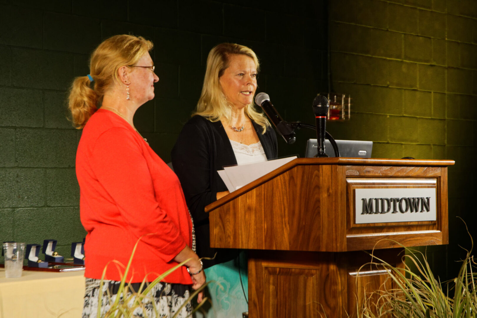 Two women standing at a podium with papers in front of them.